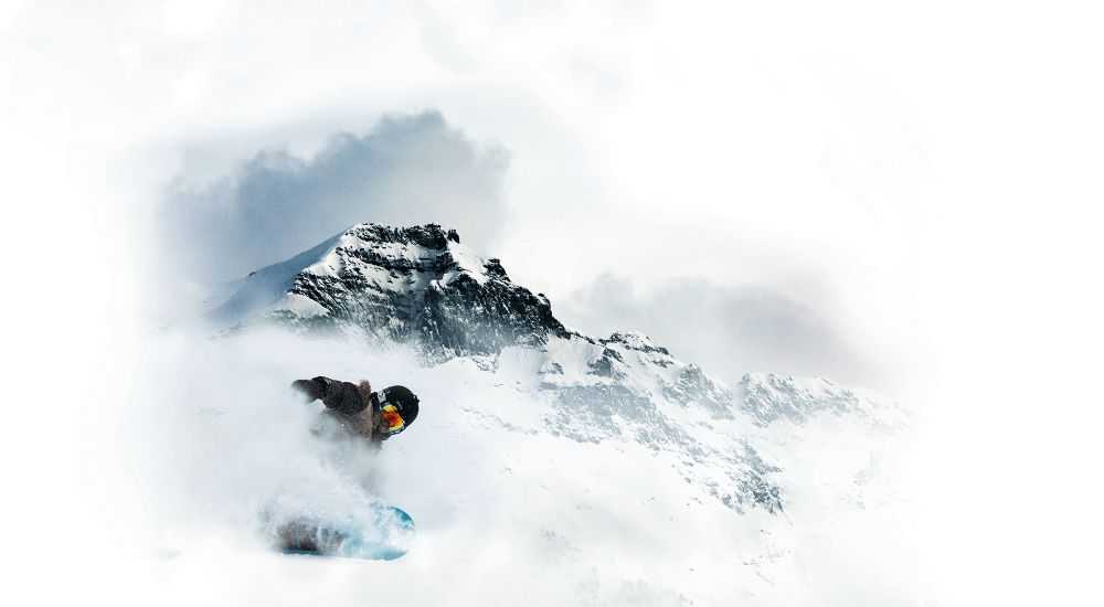 Un snowboarder desciende por una montaña cubierta de nieve, buscando la mejor protección solar facial.