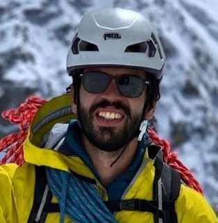 mejor-proteccion-solar-facial Un hombre con una chaqueta amarilla sonríe frente a una montaña nevada.