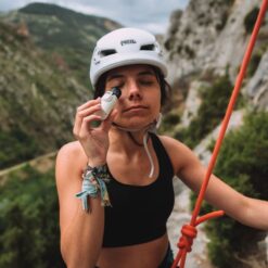 Nomad Face Bunker White Snow colgado en arnés de escalada, diseño ligero y práctico para deportistas.