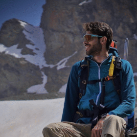 Montañista con Nomad Face Bunker Yellow Sunrise en glaciar, protector solar facial resistente al viento.
