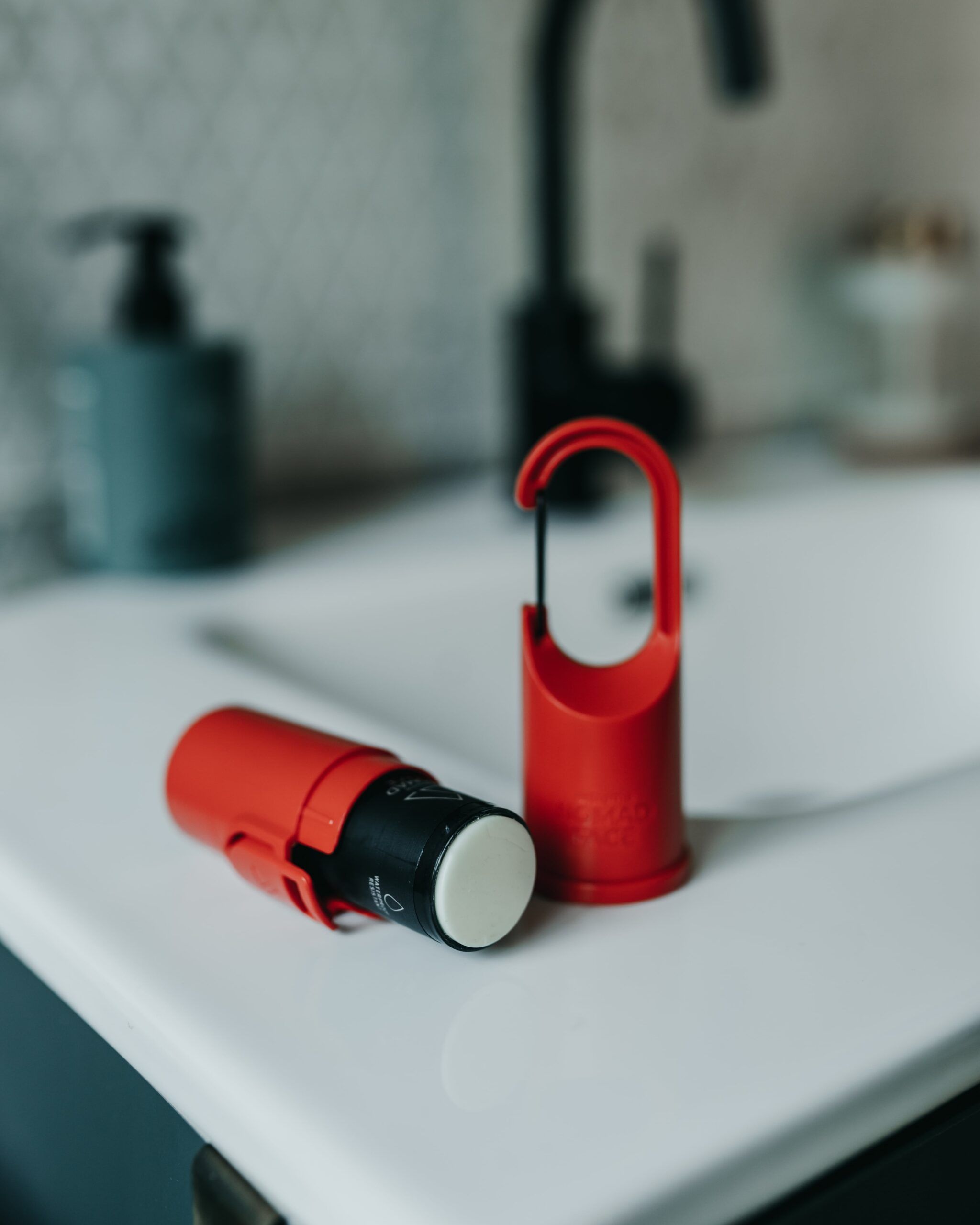 mejor-proteccion-solar-facial Aplicador de proteccion solar rojo y capsula con gancho, colocado en el lavabo del baño.