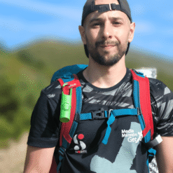 "Nomad Face Bunker Green Forest – clipado en la mochila de un excursionista durante una actividad de montaña."