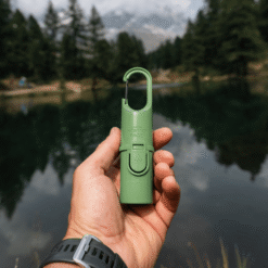 "Bunker Nomad Face Green Forest – protector solar sostenido frente a un lago rodeado de bosque, símbolo de protección outdoor."