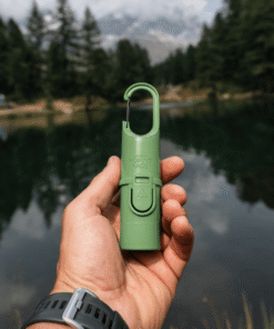 "Bunker Nomad Face Green Forest – protector solar sostenido frente a un lago rodeado de bosque, símbolo de protección outdoor."
