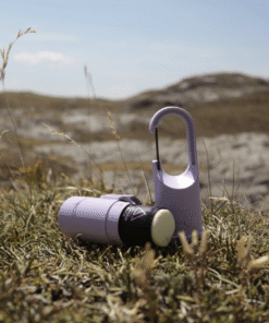"Bunker Nomad Face Purple Amethyst – protector solar recargable mostrado abierto sobre hierba en entorno de montaña."