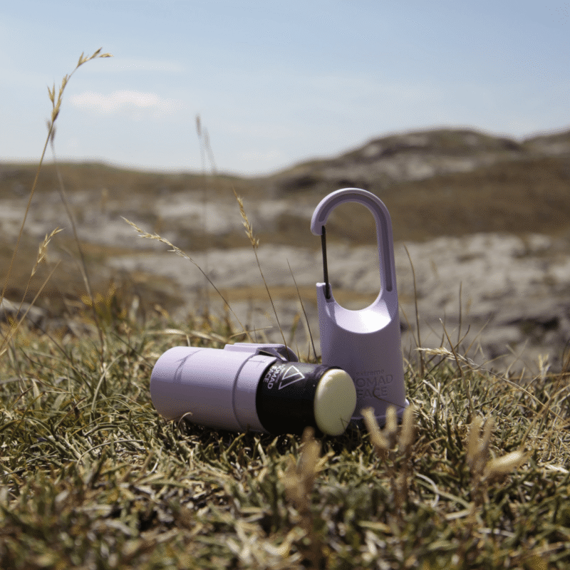 "Bunker Nomad Face Purple Amethyst – protector solar recargable mostrado abierto sobre hierba en entorno de montaña."