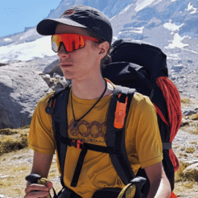 "Protector solar Nomad Face Bunker Orange Tiger – clipado en mochila de alpinista, ideal para aventuras outdoor extremas."